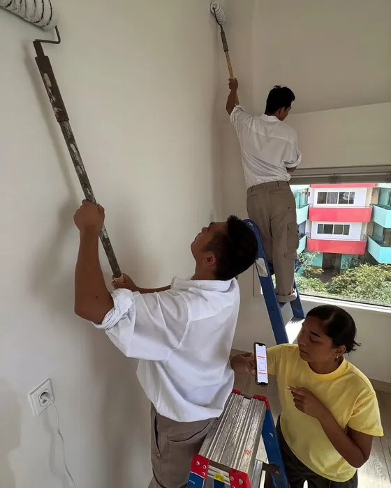 Workers painting a wall with a roller while a woman checks her phone