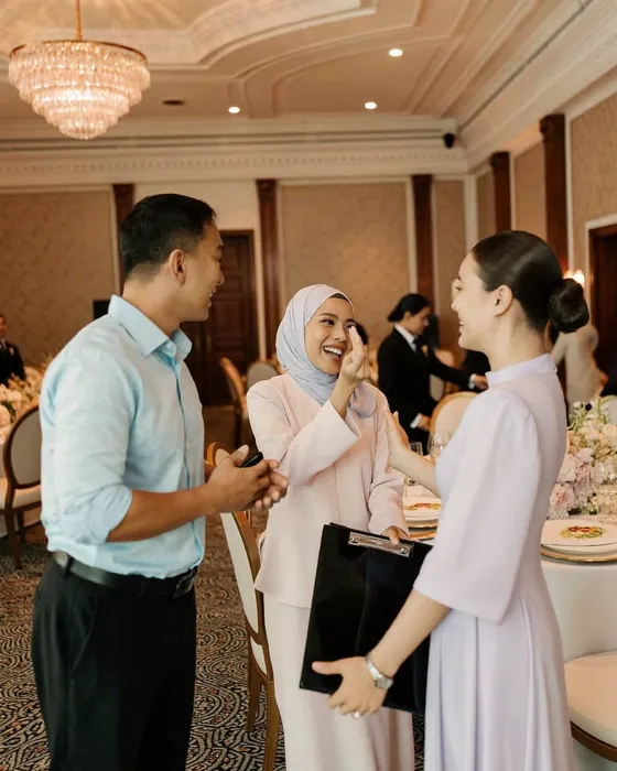 A wedding planner with a clipboard talking with a couple in a function hall